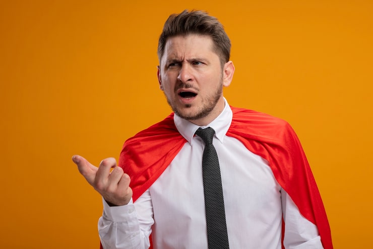 Bezpłatny plik Zdjęcie superbohater biznesmen w czerwonej pelerynie, patrząc na bok z wyciągniętą ręką, prosząc o zdezorientowany stojąc na pomarańczowym tle