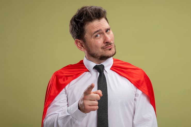 Bezpłatny plik Zdjęcie superbohater biznesmen w czerwonej pelerynie pointign z indeksem figner na camear uśmiechnięty pewny siebie stojący na zielonym tle