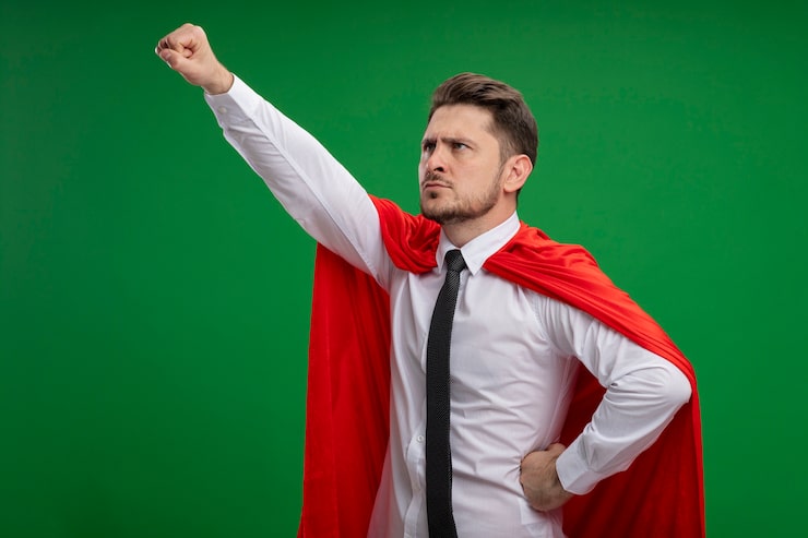 Bezpłatny plik Zdjęcie superbohater biznesmen w czerwonej pelerynie trzyma koronę, trzymając rękę w latającym geście gotowy do walki stojąc na zielonym tle