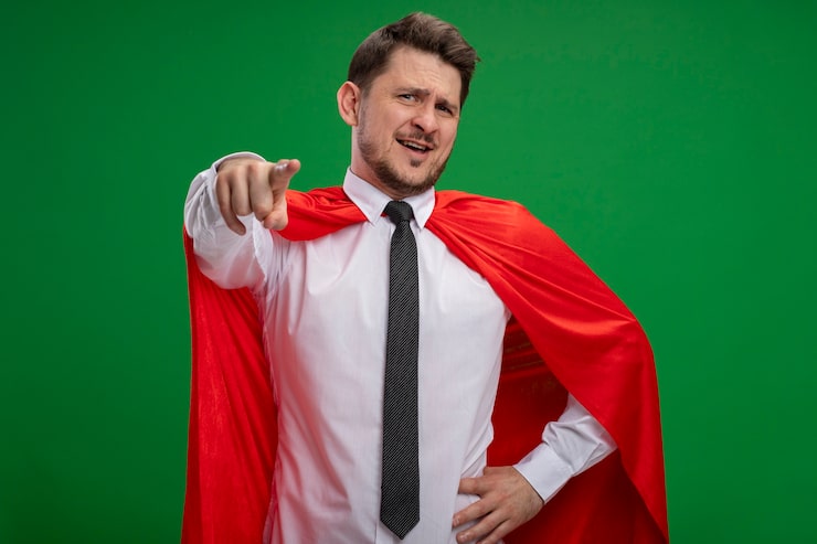 Bezpłatny plik Zdjęcie superbohater biznesmen w czerwonej pelerynie, wskazując palcem wskazującym, uśmiechając się pewnie stojąc na zielonej ścianie