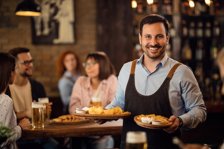 Bezpłatny plik Zdjęcie szczęśliwy kelner trzymający talerze z jedzeniem i patrzący na kamerę podczas obsługi gości w restauracji