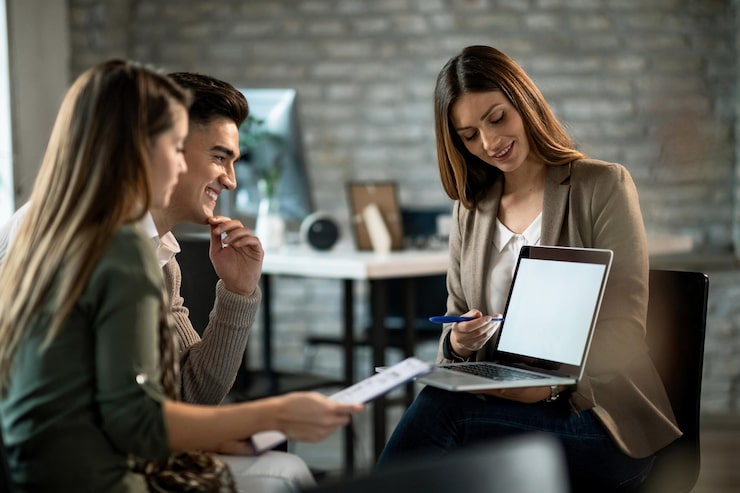 Foto gratuito agente inmobiliario sonriente usando una computadora mientras se reúne con una pareja joven y hace planes de inversión