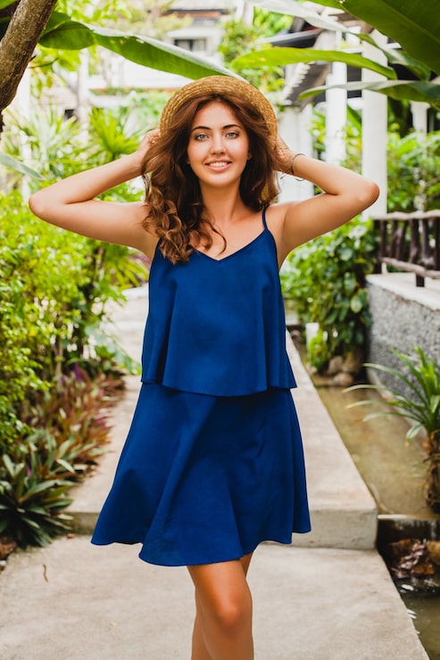 Foto gratuito atractiva mujer joven en vestido azul y sombrero de paja caminando en el hotel tropical spa villa de vacaciones en traje de estilo veraniego, sexy