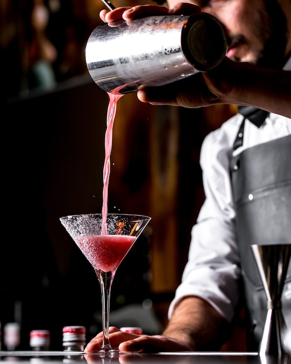 Foto gratuito bar tierna vierte un cóctel de una coctelera en una copa de martini