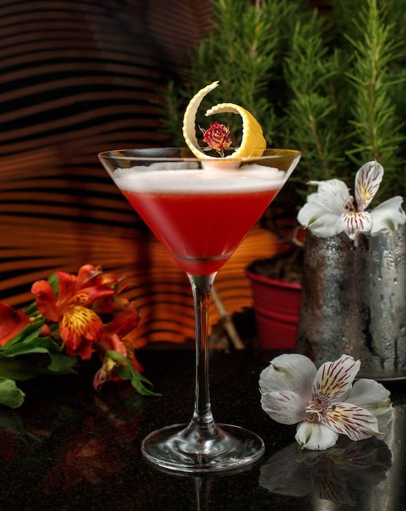 Foto gratuito bebida roja en copa de martini con guarnición de ralladura de limón en un bar iluminado con flores