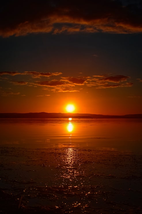 Foto gratuito bella toma vertical de la puesta de sol roja con nubes en el cielo con reflejo en el agua