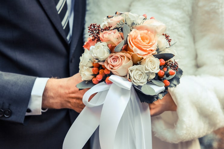 Photo Gratis bidikan jarak dekat pasangan pengantin yang memegang buket bunga dengan mawar putih dan oranye