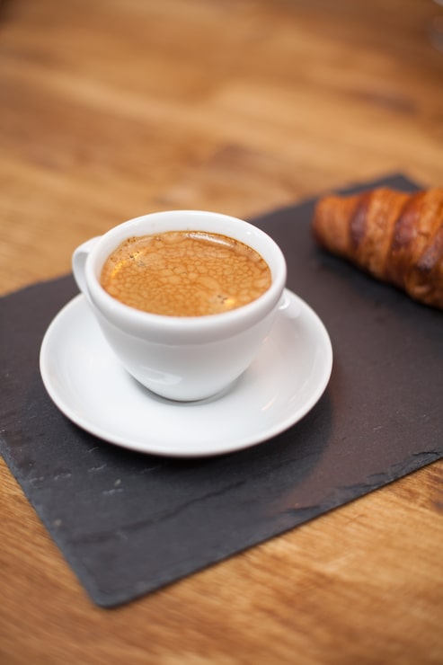 Foto gratuito café recién tostado en una taza blanca servido con un sabroso croissant. aroma de café. delicioso croissant