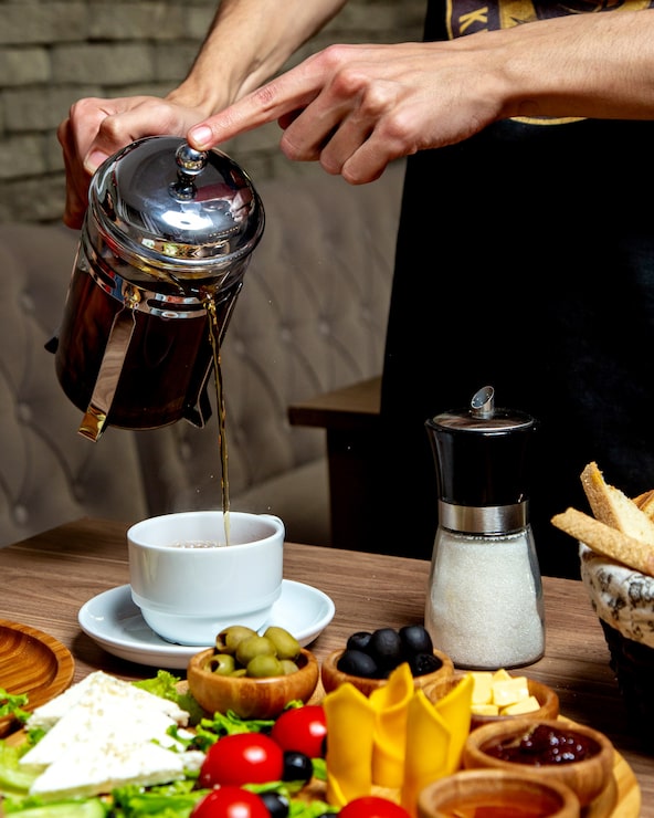 Foto gratuito camarero sirviendo té negro de prensa francesa en la mesa del desayuno