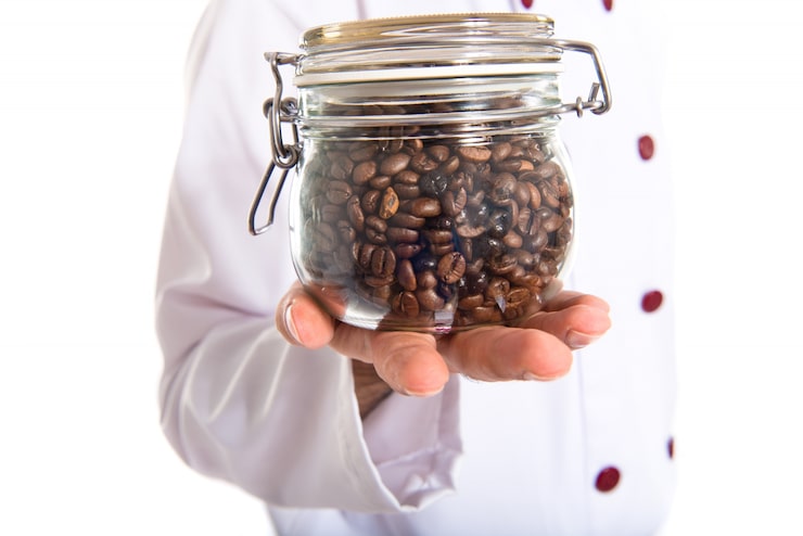 Foto gratuito chef sosteniendo jarra de vidrio con granos de café dentro
