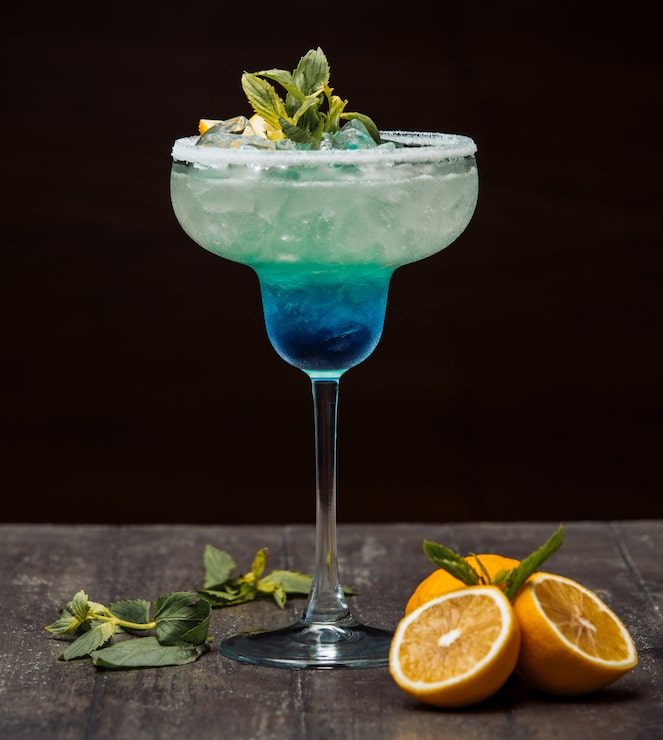 Foto gratuito cóctel azul y verde adornado con limón y menta en vaso de tallo largo