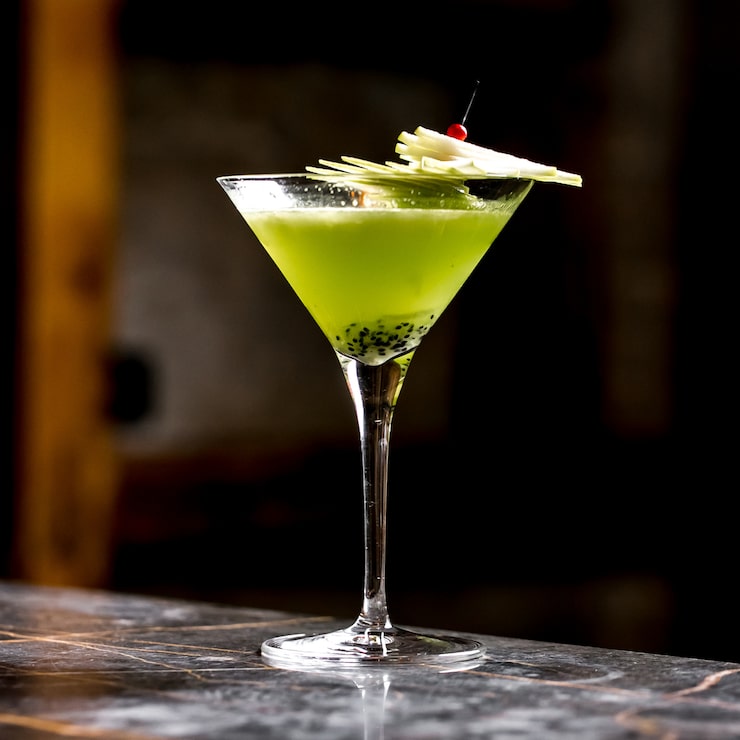 Foto gratuito cóctel de frutas de kiwi en copa de martini adornado con rodajas de manzana en una brocheta de bambú