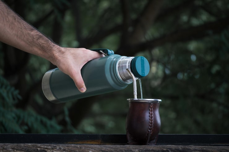 Foto gratuito disparo de enfoque selectivo de una mano vertiendo agua de un termo en una taza