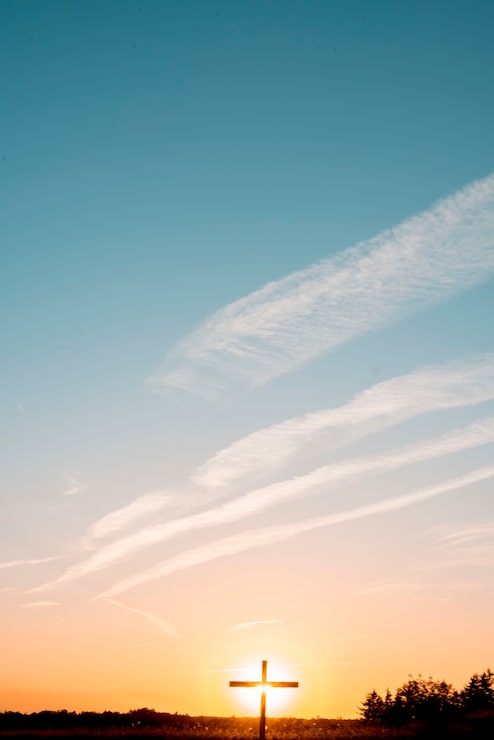 Foto gratuito un disparo vertical de una cruz de madera artesanal en el campo con el sol brillando detrás