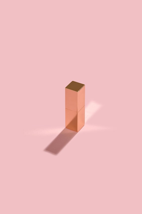 Foto gratuito estuche de lápiz labial cerrado de metal dorado sobre fondo rosa