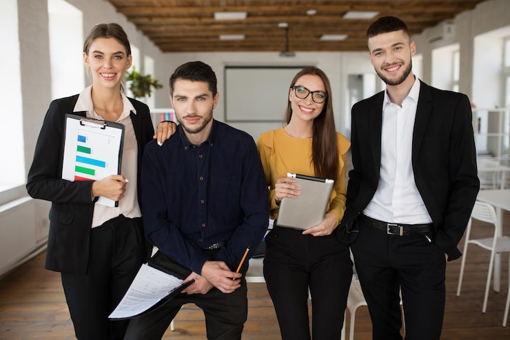 Foto gratuito grupo de jóvenes empresarios con trajes clásicos mirando juntos felizmente en cámara mientras pasan tiempo en el trabajo en una oficina moderna