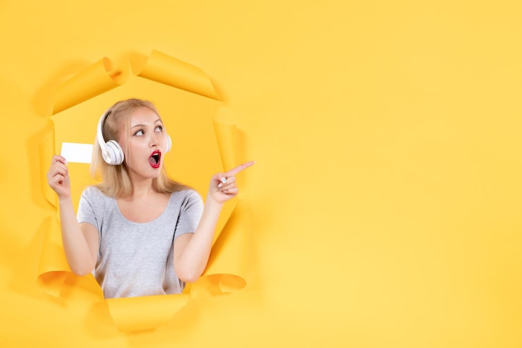 Foto gratuito hembra joven en auriculares con tarjeta de crédito en la pared amarilla