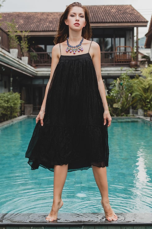 Foto gratuito hermosa mujer en elegante vestido negro largo posando en la piscina de la villa tropical, elegante estilo de verano, vacaciones, tendencia de moda, caminar descalzo