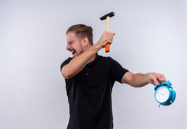 Foto gratuito hombre guapo joven decepcionado en polo negro con un martillo que va a romper el despertador en la mano con expresión agresiva en la cara de pie sobre fondo blanco.