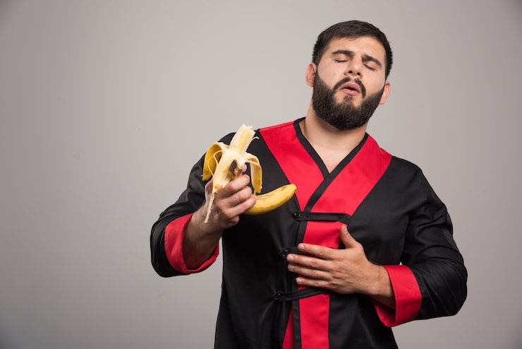 Foto gratuito joven comiendo un plátano en la pared gris.