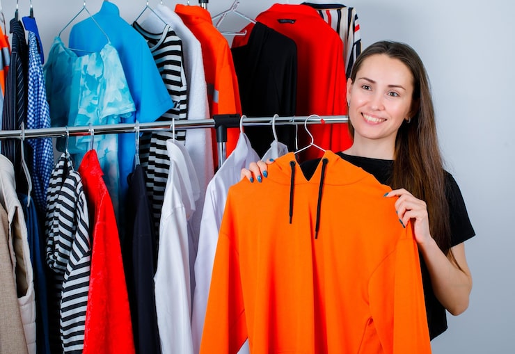 Foto gratuito la joven está sonriendo sosteniendo una sudadera en el fondo de la ropa