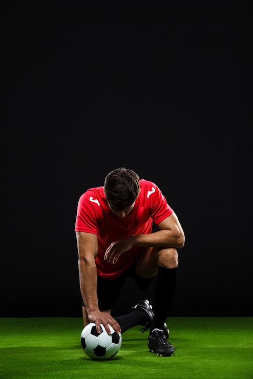 Foto gratuito jugador de fútbol con la pelota de pie en una rodilla sobre un fondo negro