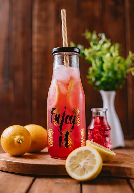 Photo Gratis koktail jeruk dengan irisan lemon dan sirup merah dalam botol dengan sedotan, tampilan vertikal