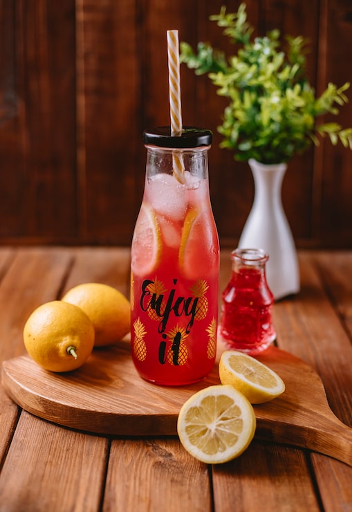 Photo Gratis koktail jeruk dengan irisan lemon dan sirup merah dalam botol dengan sedotan