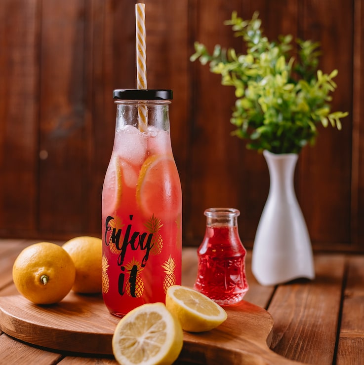 Photo Gratis koktail jeruk dengan irisan lemon dan sirup merah dalam botol dengan sedotan