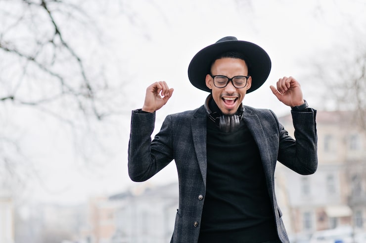 Photo Gratis model pria mulatto yang luar biasa dengan headphone tertawa dengan mata tertutup. foto outdoor pria muda afrika yang riang berdiri di langit