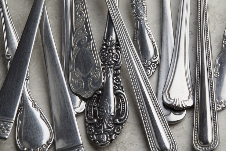 Foto gratuito un montón de tenedores y cucharas de plata con patrones antiguos en una superficie blanca