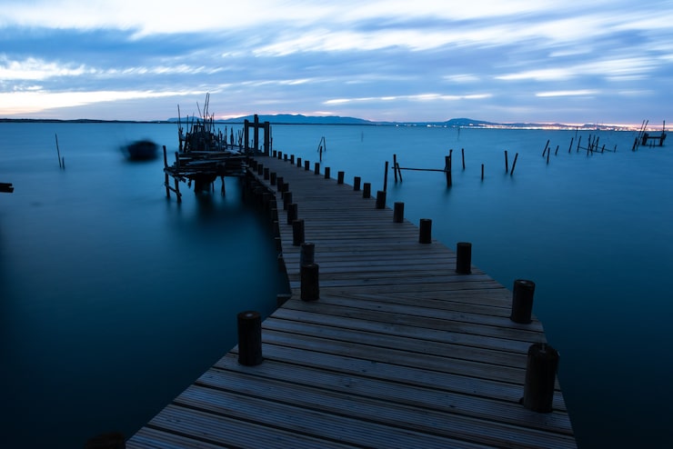 Foto gratuito muelle sobre el mar rodeado de colinas bajo un cielo nublado por la noche en portugal
