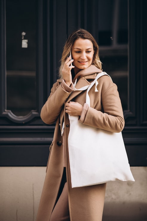 Foto gratuito mujer joven en abrigo beige con teléfono fuera de la calle