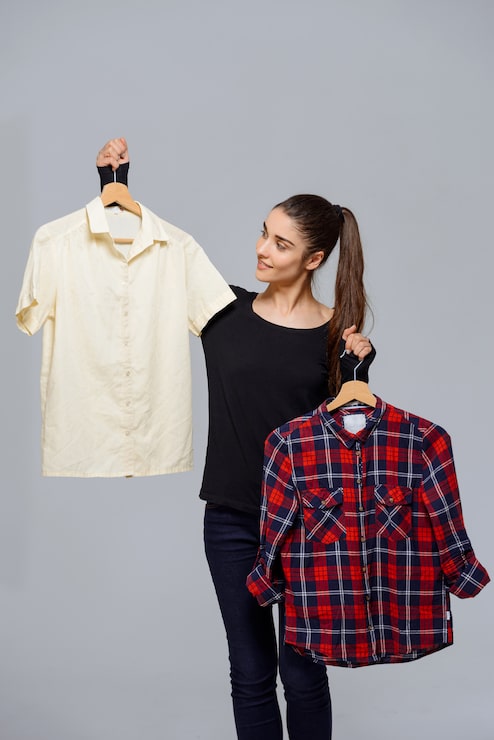 Foto gratuito mujer recogiendo atuendo, sosteniendo dos camisas eligiendo
