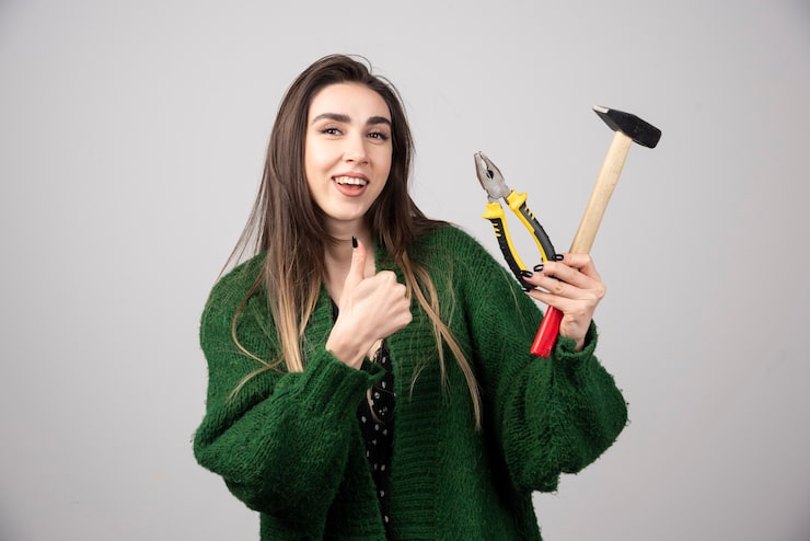 Foto gratuito niña sonriente sosteniendo un martillo con pinzas y mostrando un pulgar hacia arriba.