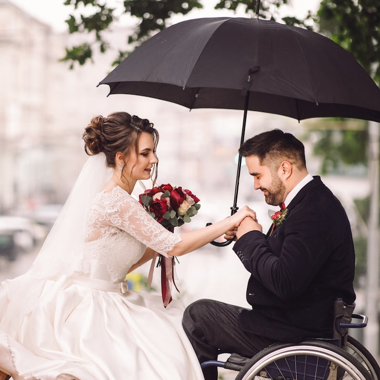 Foto gratuito la novia y el novio en la silla de ruedas se sientan besándose en el banco del parque
