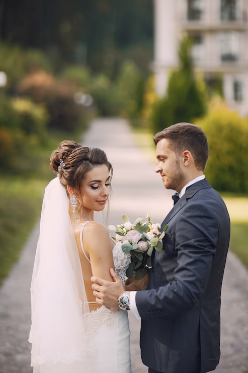 Photo Gratis pengantin wanita muda dan cantik serta suaminya berdiri di taman dengan buket bunga