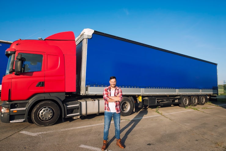 Photo Gratis potret sopir truk amerika profesional dengan pakaian kasual dan sepatu bot berdiri di depan kendaraan truk dengan trailer panjang