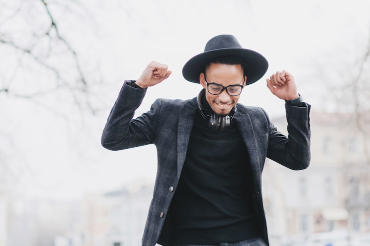 Photo Gratis pria afrika yang senang dengan senyum lembut berpose dengan tangan terangkat. potret outdoor model pria kulit hitam bahagia mengenakan setelan trendi.
