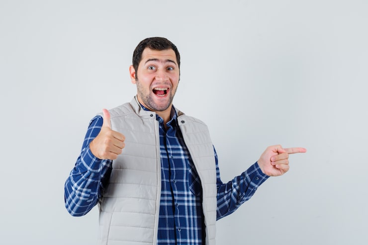 Photo Gratis pria muda memakai kemeja, jaket tanpa lengan menunjuk ke samping sambil menunjukkan jempol ke atas dan terlihat positif, tampilan depan.