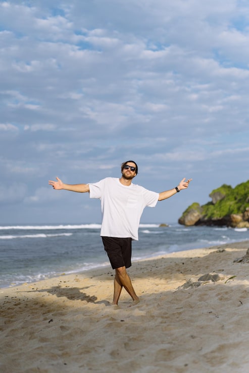 Photo Gratis pria muda tampan dengan senyum menawan memakai kacamata hitam di pantai.