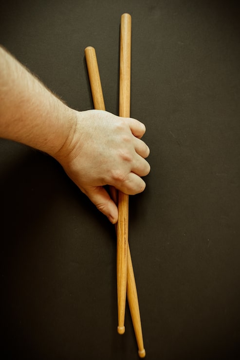 Foto gratuito primer plano vertical de la mano de una persona sosteniendo dos baquetas sobre una superficie negra