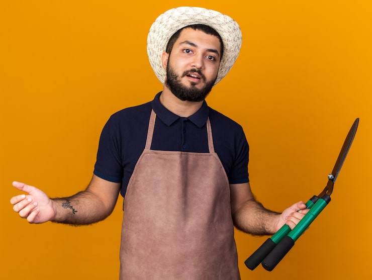 Foto gratuito sorprendido, joven, caucásico, macho, jardinero, llevando, jardinería, sombrero, tenencia, jardinería, tijeras, aislado, en, naranja, pared, con, espacio de copia
