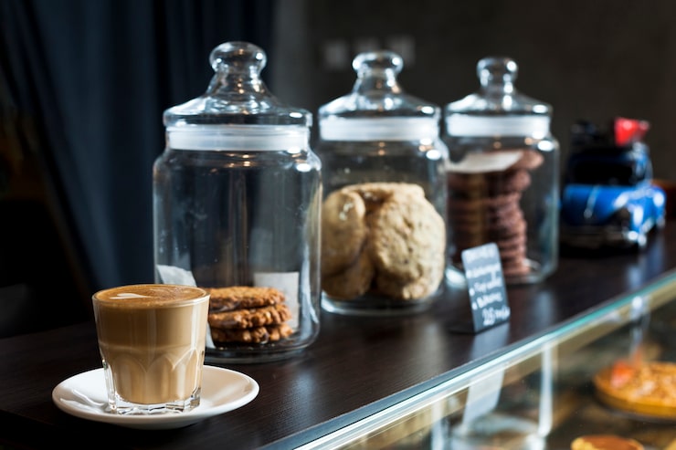 Foto gratuito tarro de varias galletas con la taza de café del latte en contador del café