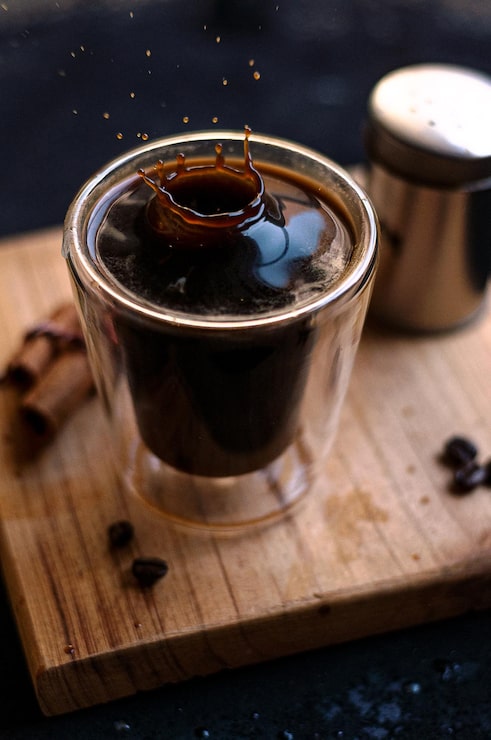 Foto gratuito taza de café espresso doble con palitos de canela y granos de café en una tabla de madera