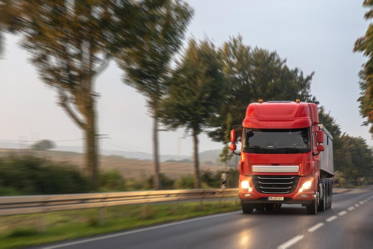 Photo Gratis truk semi merah di jalan raya pedesaan dengan lampu depan pengiriman pagi