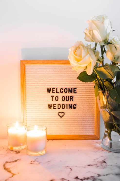 Foto gratuito velas iluminadas cerca del tablero de bienvenida de la boda y el jarrón contra el fondo blanco