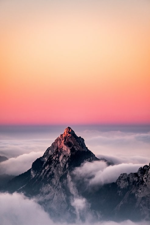 Foto gratuito vista aérea de una montaña cubierta de niebla bajo el hermoso cielo rosado