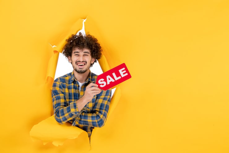 Foto gratuito vista delantera hombre joven sosteniendo escritura de venta roja en fondo amarillo rasgado