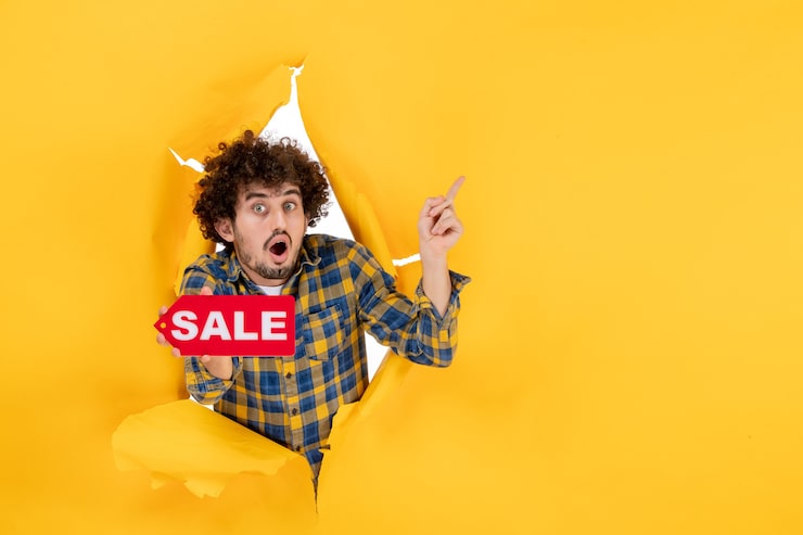 Foto gratuito vista frontal joven hombre sosteniendo venta rojo escrito sobre fondo amarillo rasgado